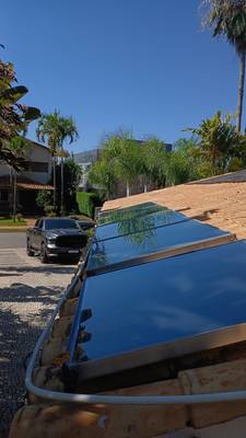 Painéis solares instalados em telhado de telha, com palmeiras ao fundo